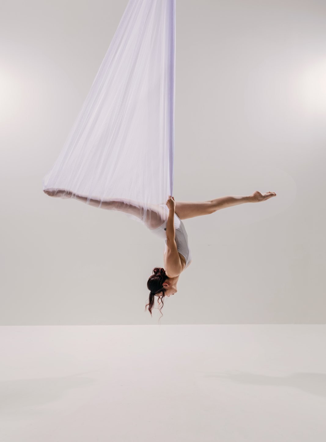 Dancer hanging inverted in sheer white mesh against a light background