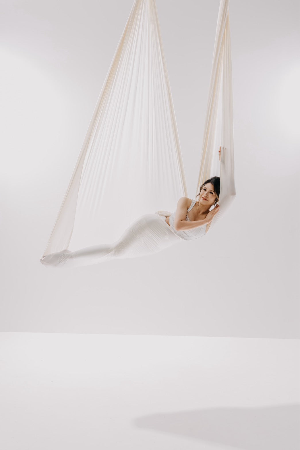 Dancer reclining in a white aerial hammock against a pale backdrop